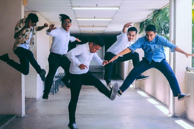 A imagem mostra cinco homens saltando felizes nos corredores de uma empresa, comemorando o sucesso em uma entrevista técnica
