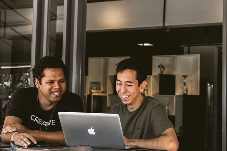 A imagem mostra dois homens representando a profissão de desenvolvedor e conversando e olhando para um computador