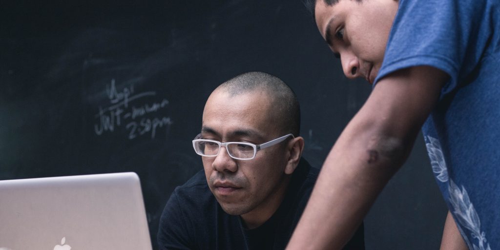 a imagem mostra dois homens, profissionais de QA, olhando para uma tela de computador