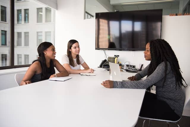 a imagem mostra três mulheres negras em um ambiente corporativo discutindo a contratação de um headhunter de ti