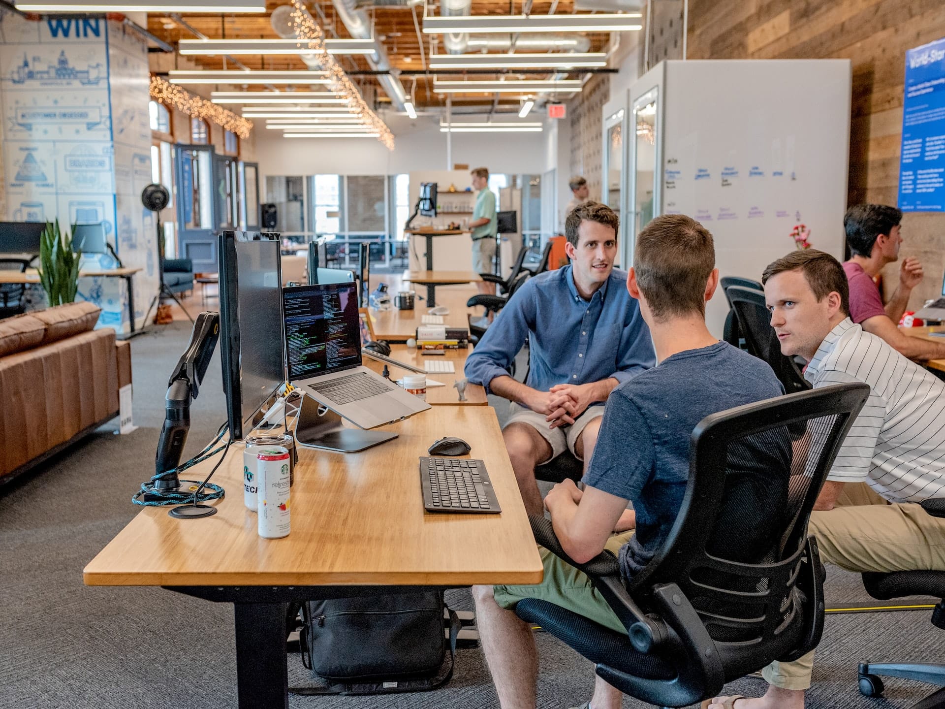 A imagem representa o ambiente corporativo de uma empresa de outsourcing, com três homens brancos sentados conversando em um escritório