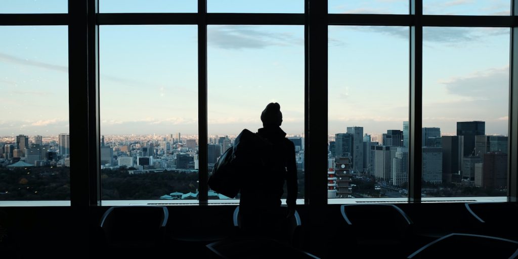 A imagem, utilizada para representar o início de uma carreira internacional, mostra um homem em um aeroporto, apreciando a paisagem através de uma janela