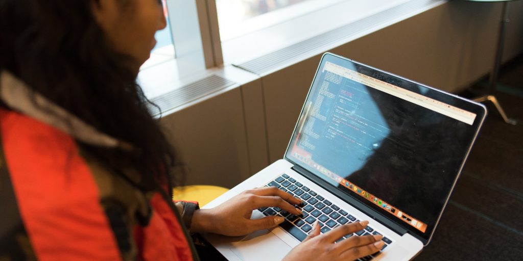 A imagem mostra uma mulher negra, com o computador sobre seu colo, atuando como uma desenvolvedora sênior