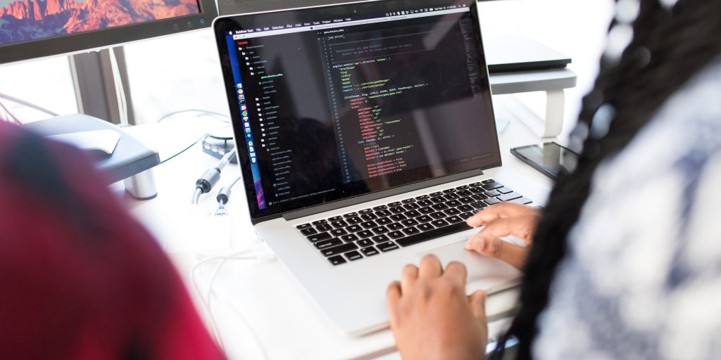A imagem mostra as mãos de uma mulher negra, na posição de desenvolvedora pleno, trabalhando em um código