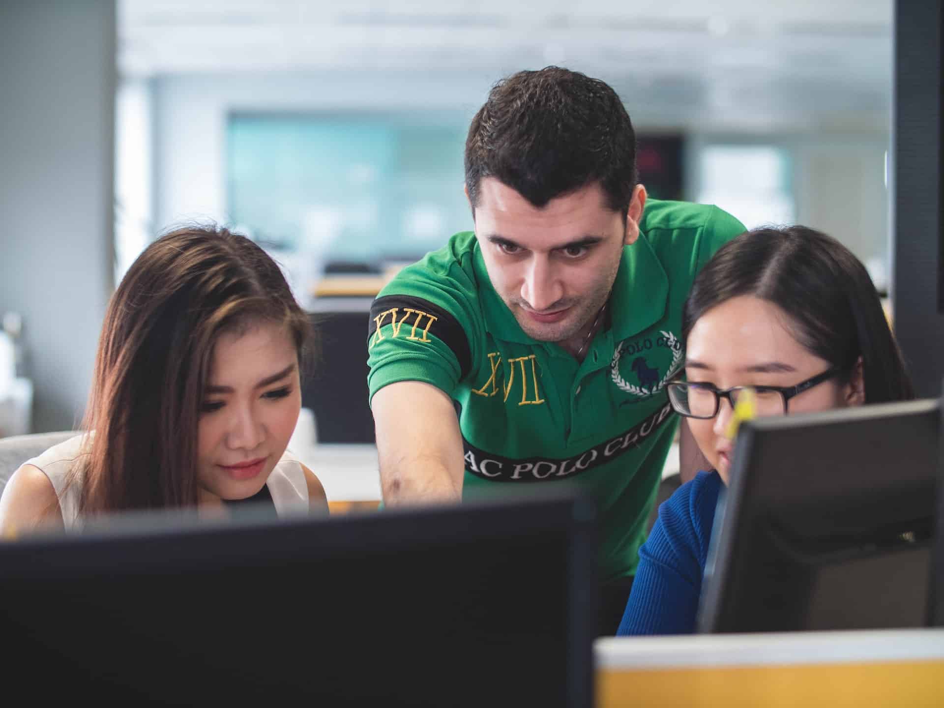 A imagem mostra um homem na posição de tech lead, guiando outras duas profissionais no desenvolvimento de software