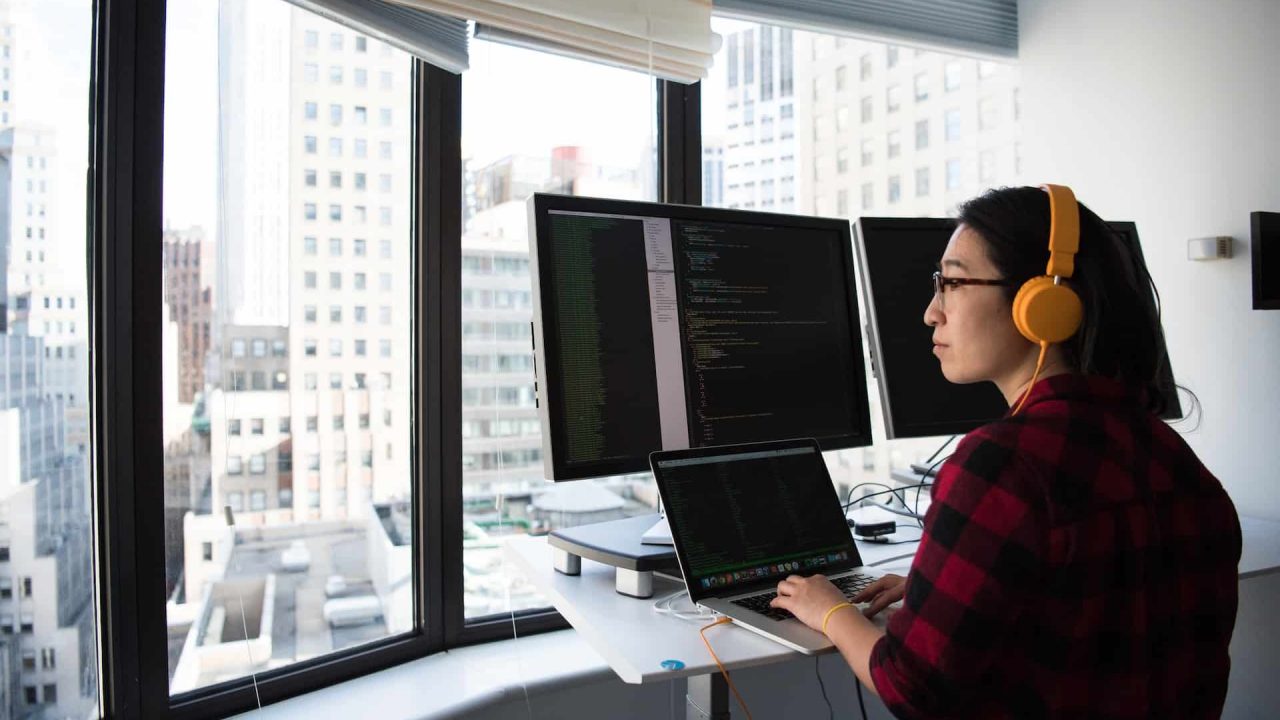 A imagem mostra uma mulher com características orientais sentada à frente de um computador atuando como desenvolvedora back-end node.js