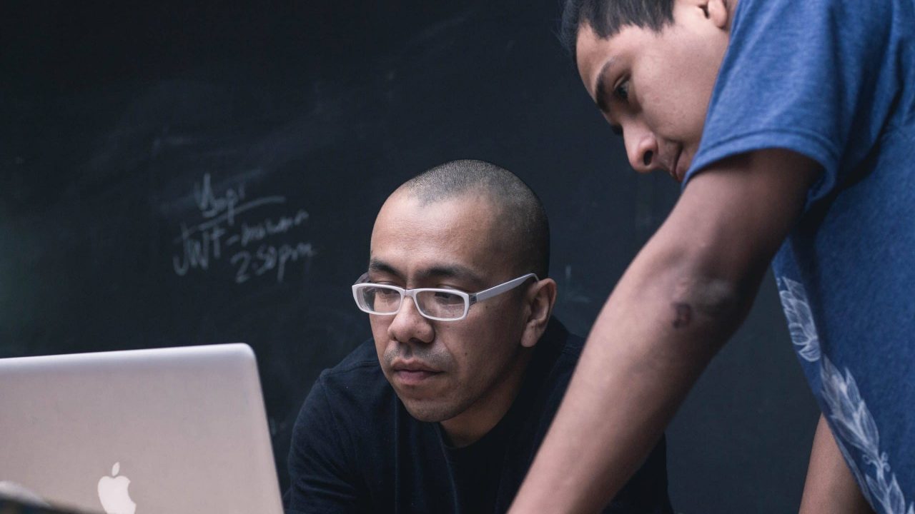 a imagem mostra dois homens, profissionais de QA, olhando para uma tela de computador