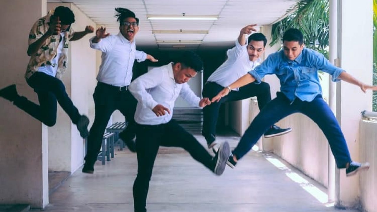 A imagem mostra cinco homens saltando felizes nos corredores de uma empresa, comemorando o sucesso em uma entrevista técnica